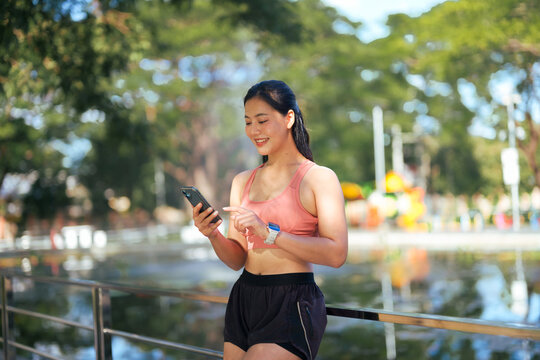 Asian woman runner using smartphone in park - Powered by Adobe