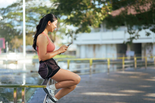 Smiling woman checking phone during outdoor workout break - Powered by Adobe