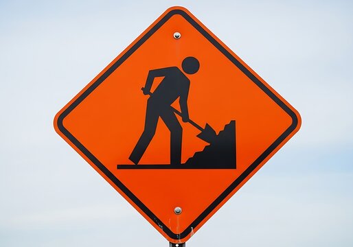 Reflective black and orange road sign showing a graphic of a person engaged in digging work on a wooden post.