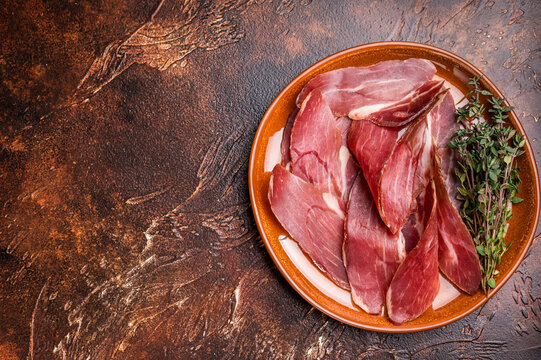 Balkan Prsut prshut, sliced cured pork meat ham on plate. brown background. top view