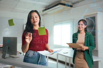 Businesswomen brainstorming ideas on glass board in office