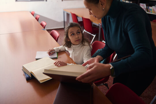 Young Girl Receives Help From Teacher Reading Books In Library Classroom Setting