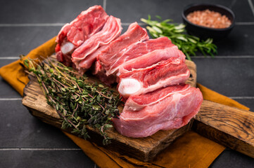 Fresh lamb rack rib pieces, mutton meat with thyme on wooden board. black background. top view