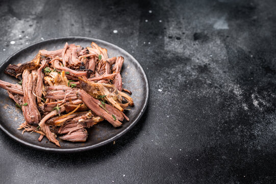 A tantalizing plate of pulled brisket, slow-cooked to perfection, drizzled with barbecue sauce for added flavor. black background. top view