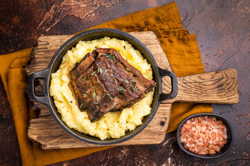 Close-up of tender beef short ribs, beautifully caramelized and resting on a bed of creamy mashed potatoes, creating an inviting culinary scene. brown background. top view