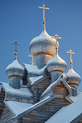 Wooden domes covered with snow and an Orthodox cross of the church against the blue sky in winter.