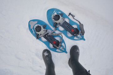 Snowshoes in the snow and a person's feet in boots in winter