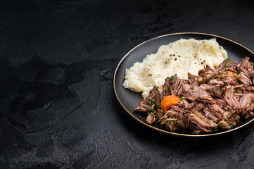 Beef stew with mashed potatoes, carrots and herbs on a plate isolated. black background. top view
