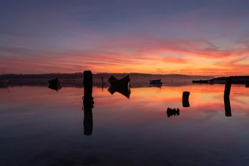 Fototapete Reflection Sunset reflected in a mirror-like body of water with silhouettes of boats and other elements in an atmosphere of peace and tranquility.  © ANTONIO