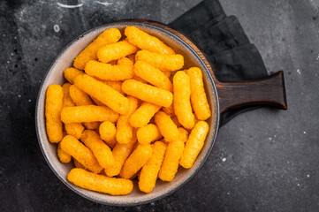Deliciously addictive cheese flavored corn puffs, beautifully arranged on a plate. black background. top view