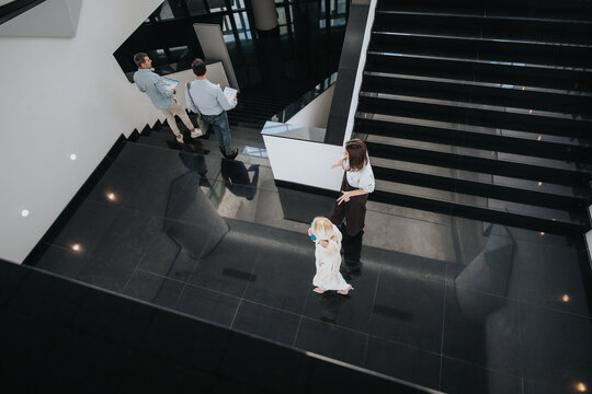 A sleek office lobby shows a mother and child on the lower level while colleagues converse near the stairs on the upper level.