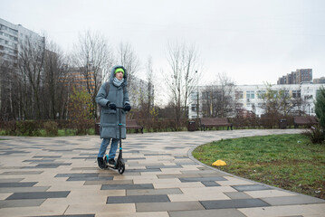 A teenage boy rides a scooter home from school in cold weather.