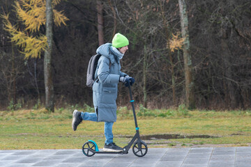 A teenage boy rides a scooter home from school in cold weather.