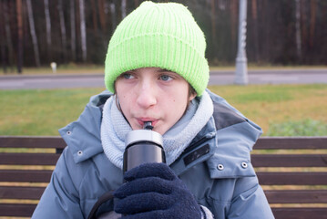 Portrait of a teenage boy in a jacket and hat, the child drinks water from a plastic bottle.