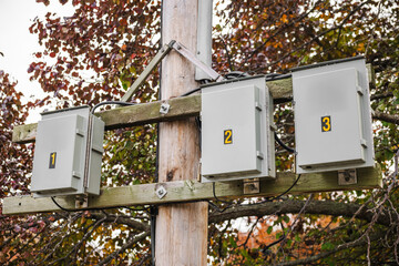 Numbered electrical junction boxes mounted on a wooden utility pole with cables and autumn foliage in the background, part of outdoor power infrastructure.