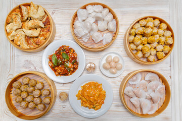 Variété de plats chinois : bouchées, raviolis vapeur, raviolis grillés, poulet épicé, litchis au sirop sur assiettes blanches et paniers.  Vue 90°. Cuisine chinoise. Traiteur chinois.