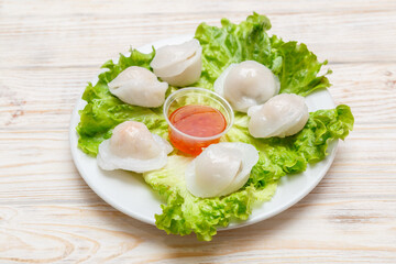 Raviolis aux Saint-Jacques sur assiette blanche avec feuille de salade et sauce piquante. Cuisine chinoise. Traiteur chinois.