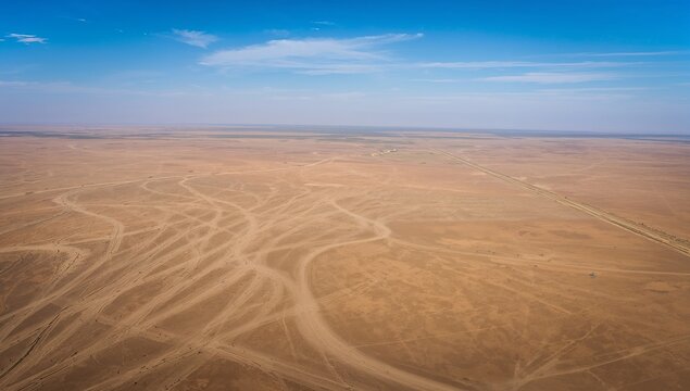 Revealing vast desert plain showing winding vehicle tire tracks from aerial view, unpaved road