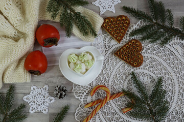 Christmas backdrop: a mug with sweets, persimmons, and cookies on a white lace napkin