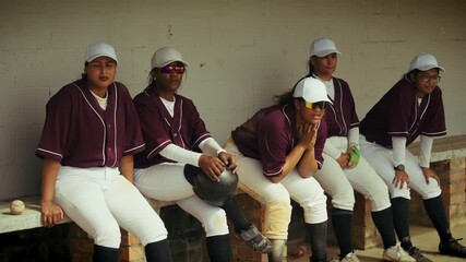 Female baseball players watch the game intently from the dugout bench. The team is focused and ready for their next play, showcasing dedication and spirit. - Powered by Adobe