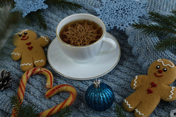 Christmas background: a tea mug with a decorative snowflake on a blue knitted piece with gingerbread cookies and a Christmas tree ornament