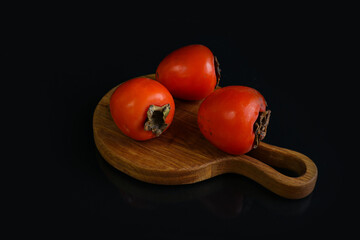 Orange persimmon on a wooden board against a dark background