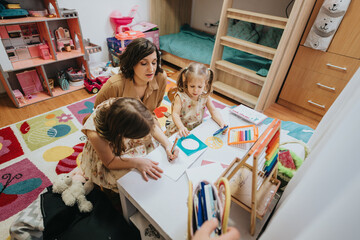A warm moment of bonding as a mother and her two daughters engage in creative drawing activities together in their colorful and tidy playroom, emphasizing family connection and artistic development.