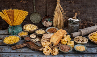 Different types of uncooked pasta on rustic wooden table, in the spoons, cutting board and bowls 