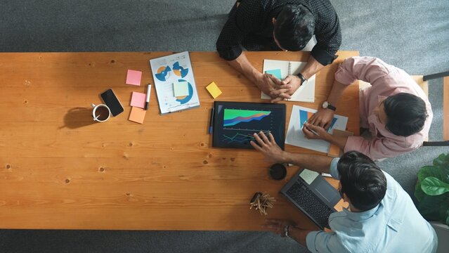 Top view of skilled project manager talking about financial graph to investors while sitting at meeting table with data analysis document. Diverse team discussing and brainstorming idea. Convocation. - Powered by Adobe