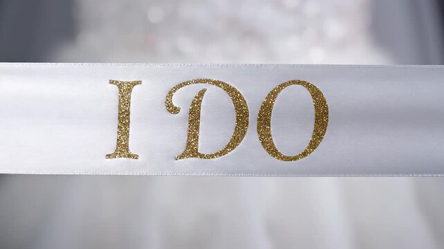 Bride's celebratory 'I Do' sash with gold glitter lettering displayed on a wedding dress
