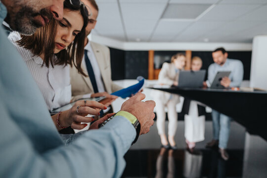 A diverse group of coworkers gathers around a table, examining papers and a laptop as they discuss plans and share ideas in a bright, contemporary workspace.