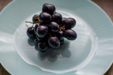 Glossy dark grapes on pale blue plate with soft lighting and textured background.