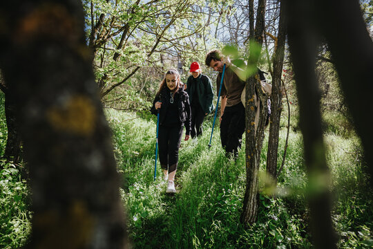 A small group of friends explores a grassy forest trail with walking sticks, enjoying nature and outdoor activity.