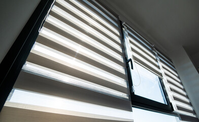 Sunlit zebra roller blinds on modern window creating striped light patterns across home interior surfaces © Volodymyr_sh