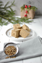 Creamy sunflower halva cut into rustic cubes on a white plate with seeds and festive evergreen accents.