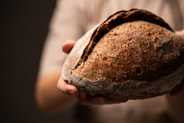 Artisan whole-grain bread held in hands, showcasing rustic crust and handcrafted bakery tradition