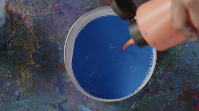 Orange Farbe wird in blaue Fl&uuml;ssigfarbe gegeben &ndash; k&uuml;nstlerischer Mischprozess im Studio mit starkem Kontrast, Tropfenbewegung und kreativer Farbkombination