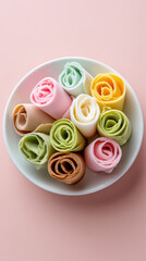 Colorful rolled desserts arranged in a white bowl on a pink background showcasing various flavors and textures