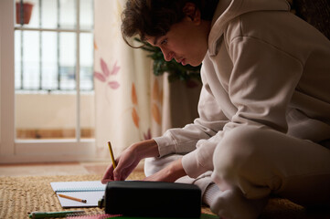 Teenage Boy Studying at Home, Writing in Notebook, Focused on Homework, Quiet Moment