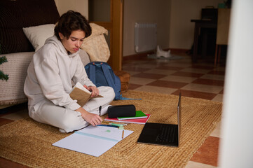 Teenage Boy Studying at Home With Laptop, Notebook, and Backpack