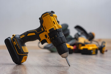 Cordless drill surrounded by various power tools on a wooden floor. Construction equipment, DIY...