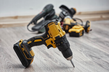 Yellow cordless drill with additional power tools in the background. Construction work, home improvement, mechanical tasks and modern workshop equipment.