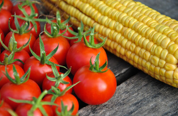 ripe tomatoes with green tails and young corn on a wooden table
