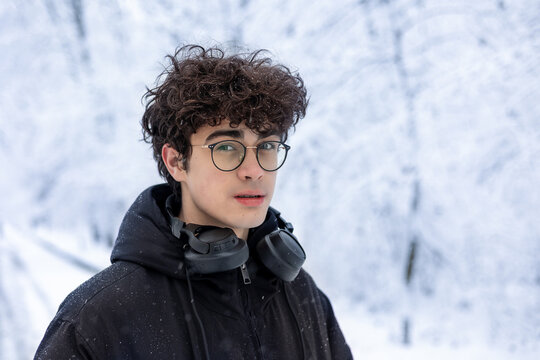 Teenager in Winter Forest Wearing Headphones — Winter Lifestyle Portrait of Gen Z Boy Outdoors. Young Man with Headphones in Snowy Park — Winter Fashion, Teen Emotions. Curly-Haired Teen Boy in Glasse