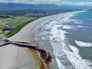 
Aerial drone view of the Bertioga coastline, Brazil. Waves with white foam reaching the beach. Meeting of dark rainwater and seawater.