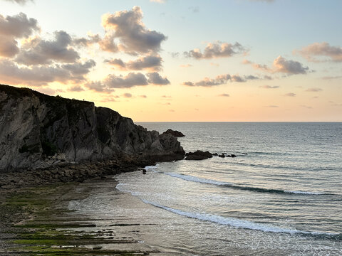Calm ocean waves rolling toward the shore at sunset with warm sky colors and coastal rock formations