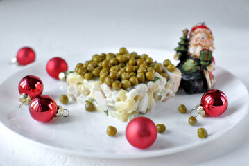 Holiday salad topped with green peas on a white plate surrounded by red baubles and a small Santa figurine.