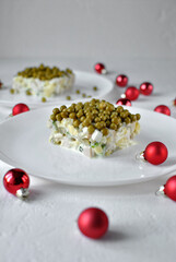 A square serving of creamy pea salad on a white plate surrounded by red Christmas baubles.