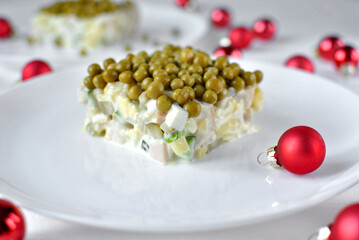 A creamy layered pea and vegetable salad square served on a white plate with red Christmas baubles for a festive table.