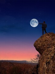 man standing on the moon. Reaching for the Moon on a Mountain Cliff